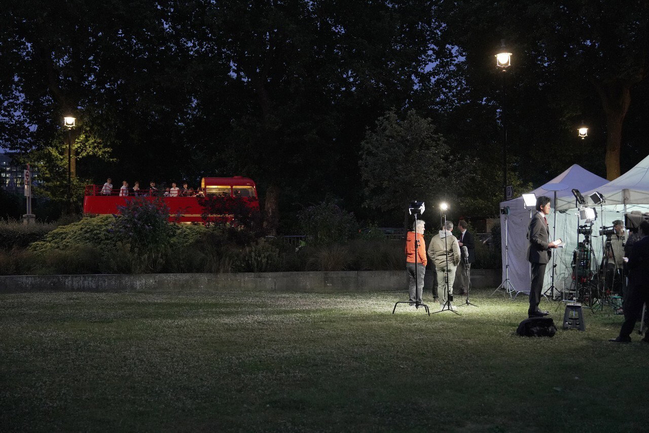 Several people standing in a park at night with lighting rigs visible