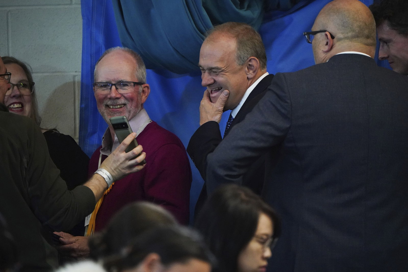 Man smiling while someone shows him a phone 